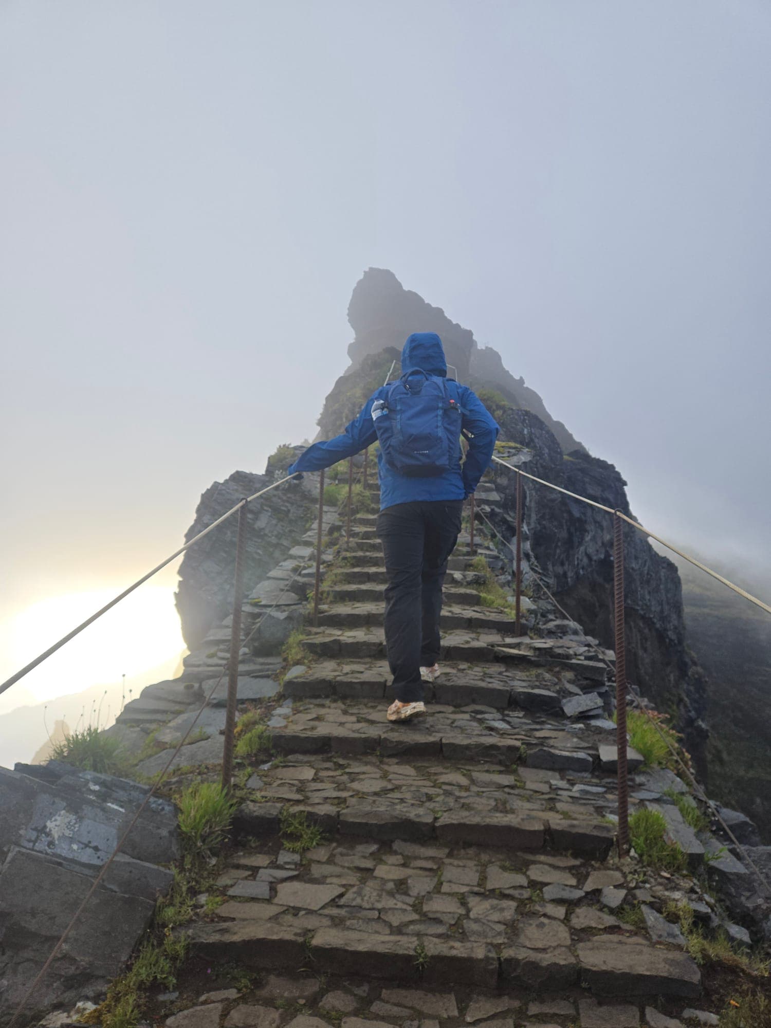 Hiker on a stone staircase along a misty mountain ridge