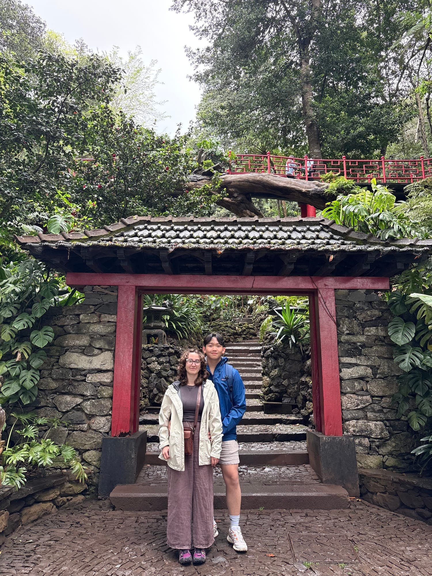 Two friends under a red wooden gate in a lush tropical garden